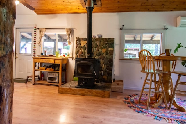 interior space with wooden ceiling, a wood stove, an AC wall unit, and wood finished floors