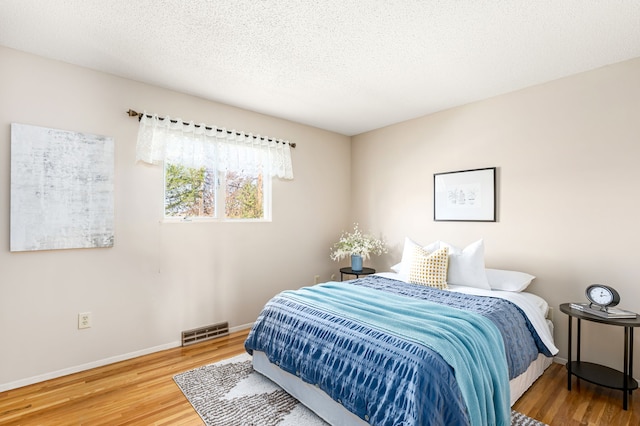 bedroom with a textured ceiling, baseboards, visible vents, and wood finished floors