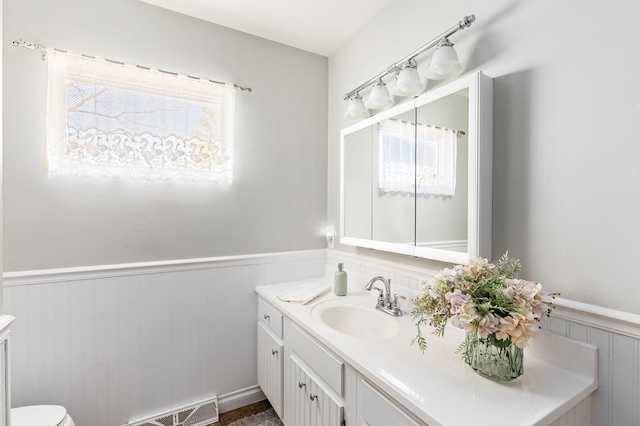 bathroom featuring a wainscoted wall, toilet, and vanity