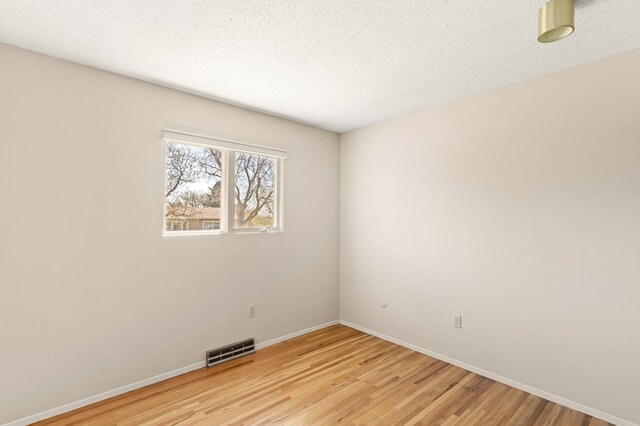 spare room with light wood finished floors, a textured ceiling, visible vents, and baseboards