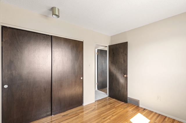 unfurnished bedroom featuring light wood-type flooring, baseboards, a closet, and visible vents