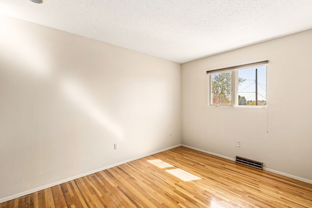 spare room featuring light wood-type flooring, baseboards, visible vents, and a textured ceiling