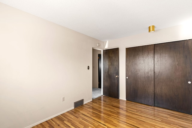unfurnished bedroom with multiple closets, baseboards, visible vents, and wood finished floors