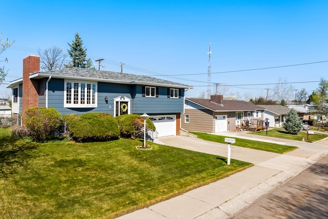 raised ranch featuring concrete driveway, a chimney, a front lawn, and an attached garage