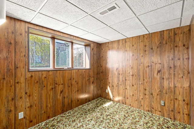 spare room with a drop ceiling, wood walls, and visible vents