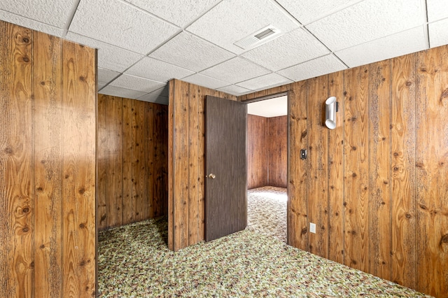 interior space with a paneled ceiling, wood walls, and visible vents