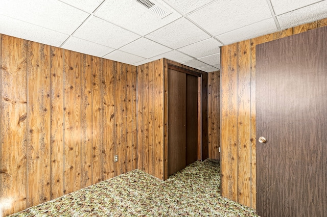 interior space with a drop ceiling, wooden walls, visible vents, and carpet