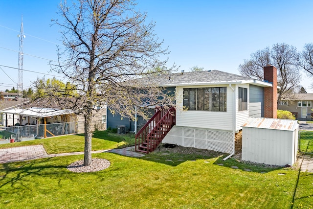 rear view of house featuring fence, a storage unit, an outbuilding, cooling unit, and a lawn