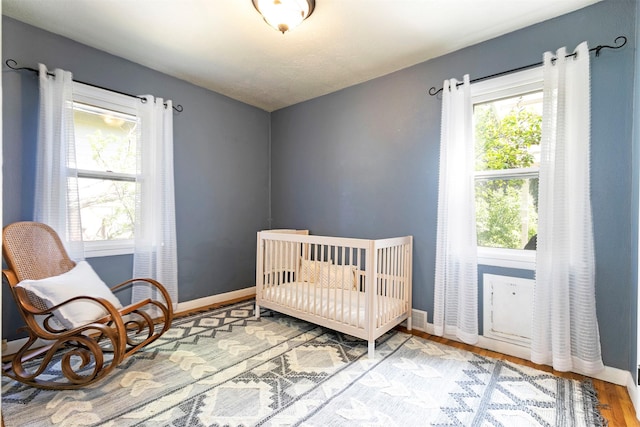 bedroom with baseboards, a crib, and wood finished floors