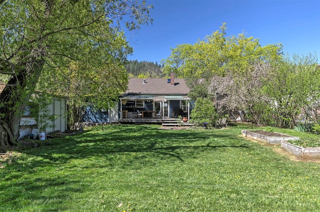 rear view of house with a storage unit, a chimney, a lawn, a wooden deck, and a vegetable garden