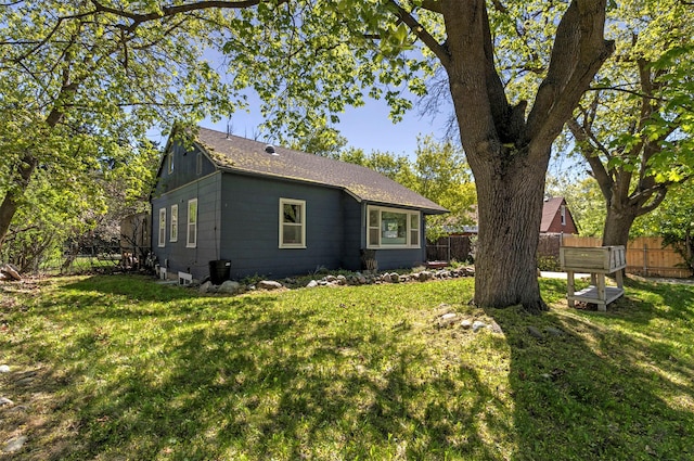 view of property exterior with roof with shingles, fence, and a lawn