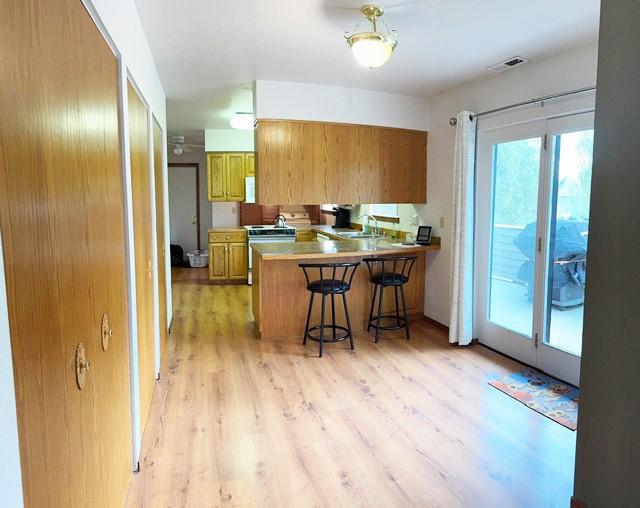 105 Garden Dr Unit D, Kalispell, MT 59901 - kitchen with brown cabinetry, visible vents, a kitchen bar, a peninsula, and light wood-style floors
