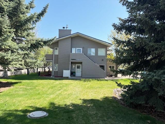 105 Garden Dr Unit D, Kalispell, MT 59901 - back of house featuring a chimney, fence, and a lawn