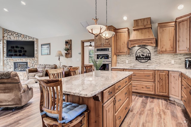 617 Mcclellan Creek Rd, Clancy, MT 59634 - kitchen featuring custom exhaust hood, vaulted ceiling, a fireplace, light wood finished floors, and double oven