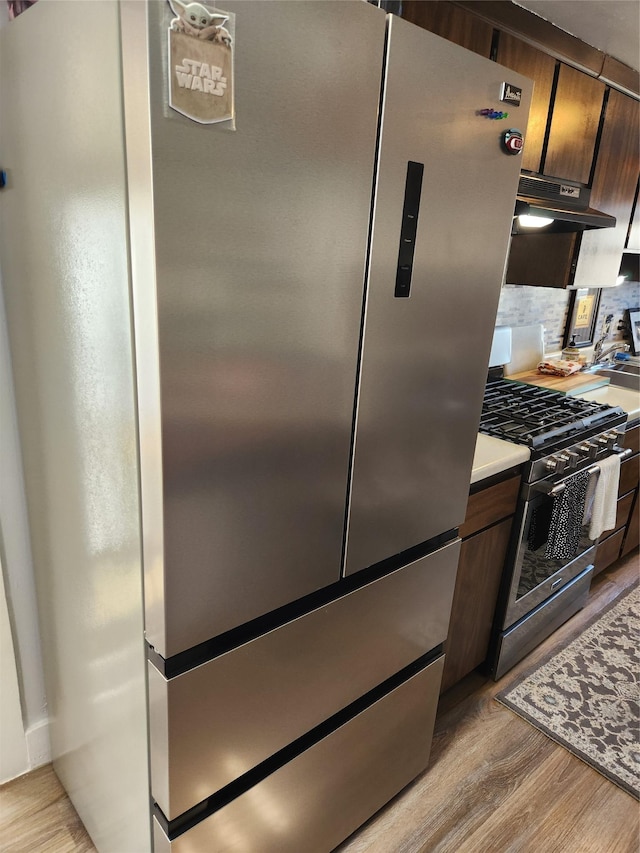 kitchen with stainless steel appliances, under cabinet range hood, light wood finished floors, and backsplash