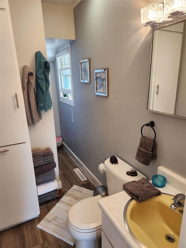 half bathroom featuring toilet, wood finished floors, and vanity