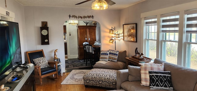 living area with arched walkways, wood finished floors, ceiling fan, and a textured ceiling