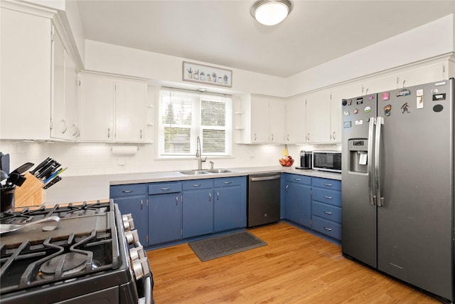 kitchen with stainless steel appliances, a sink, blue cabinetry, light countertops, and decorative backsplash