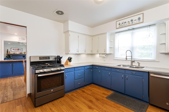 kitchen featuring appliances with stainless steel finishes, a sink, blue cabinetry, tasteful backsplash, and light wood finished floors