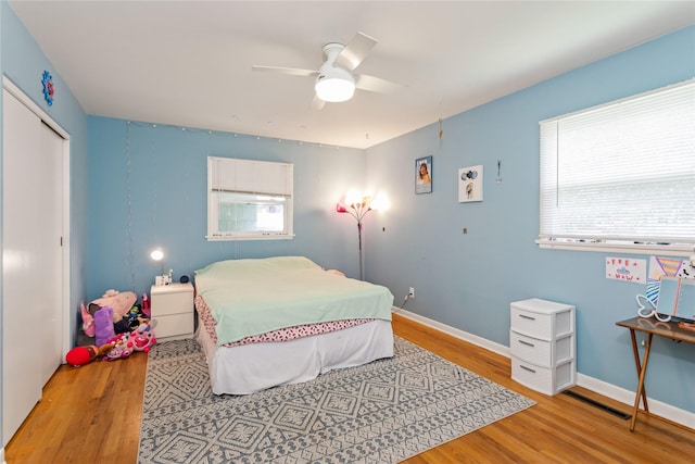 bedroom with wood finished floors, multiple windows, a closet, and a ceiling fan