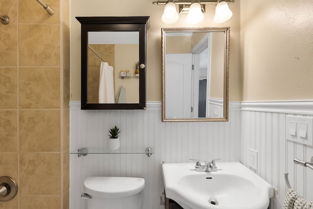full bath featuring a sink, a shower with curtain, a wainscoted wall, and toilet