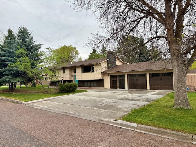 bi-level home with driveway, a garage, a front yard, and a chimney