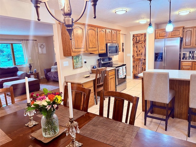 kitchen with stainless steel appliances, light countertops, hanging light fixtures, light tile patterned flooring, and brown cabinets