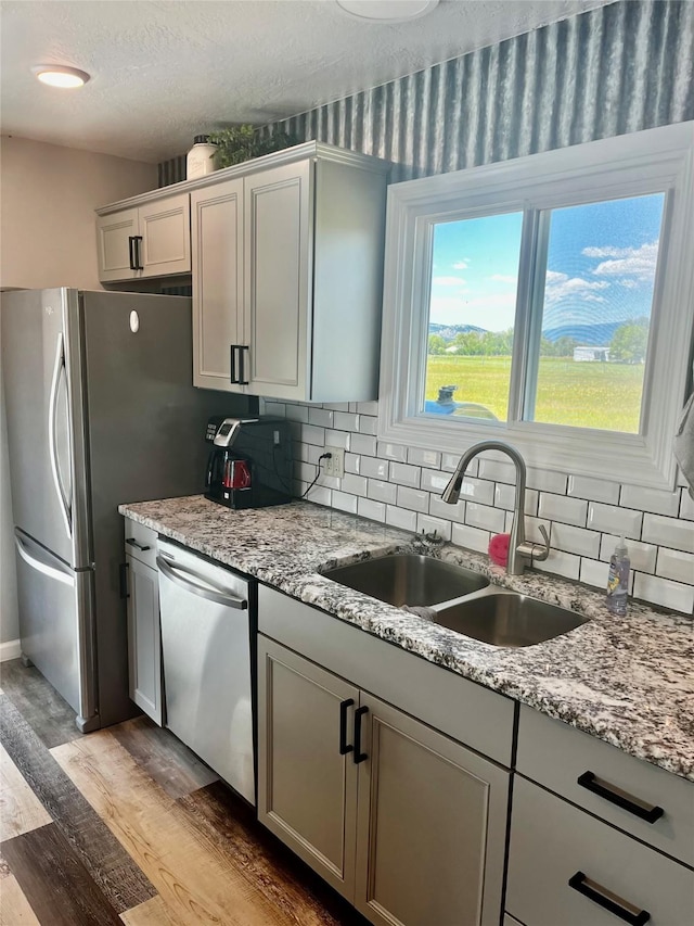 kitchen featuring stainless steel appliances, a sink, light wood-style floors, decorative backsplash, and light stone counters