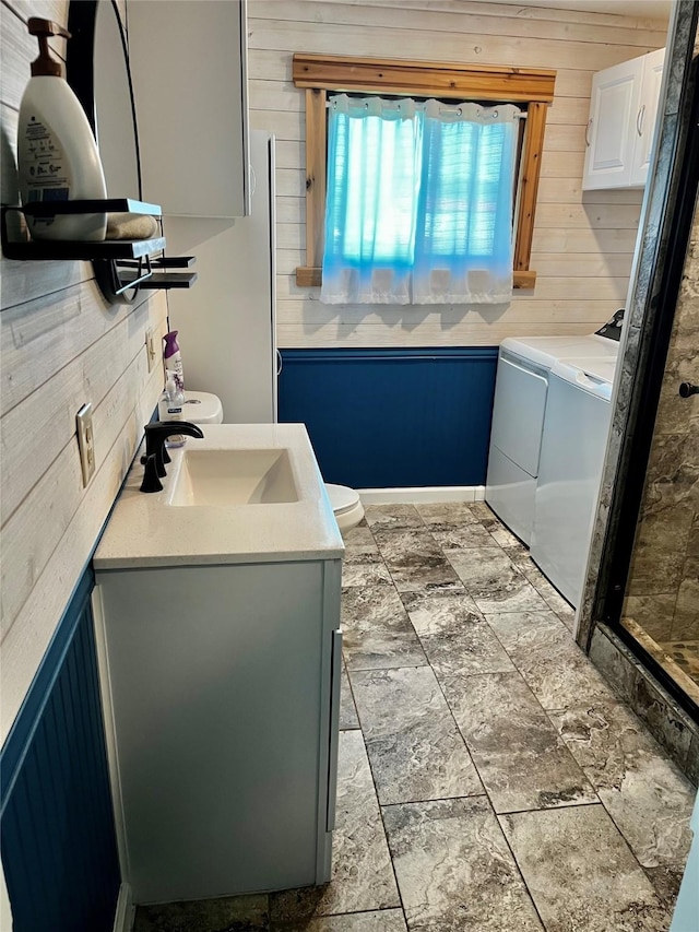 bathroom featuring washer and dryer, vanity, wooden walls, and stone finish floors