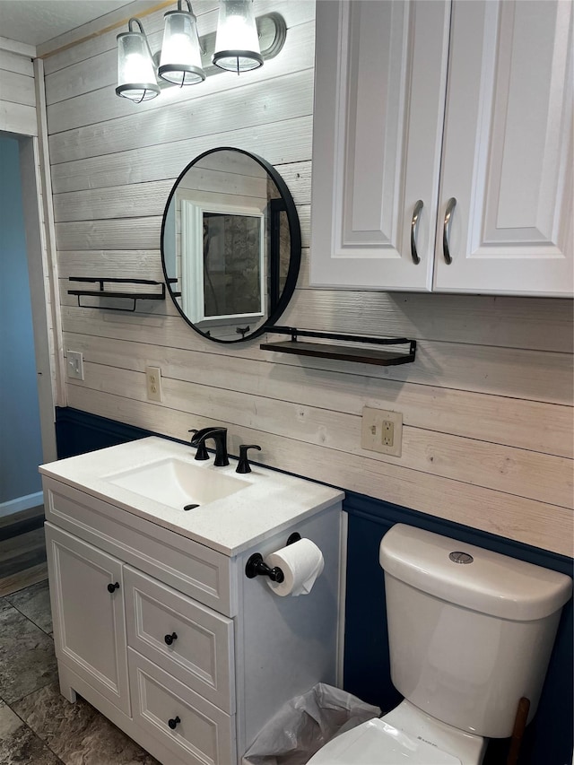 bathroom with wooden walls, toilet, and vanity