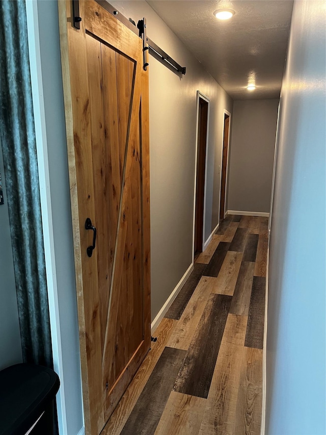 hall featuring a barn door, wood finished floors, and baseboards