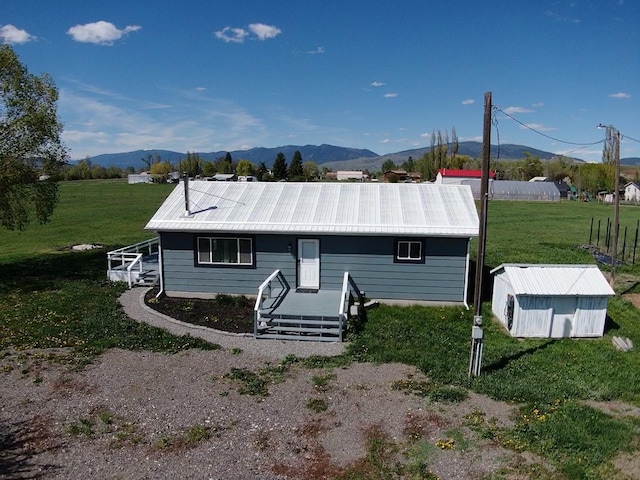 back of property with a mountain view, a yard, metal roof, and an outbuilding