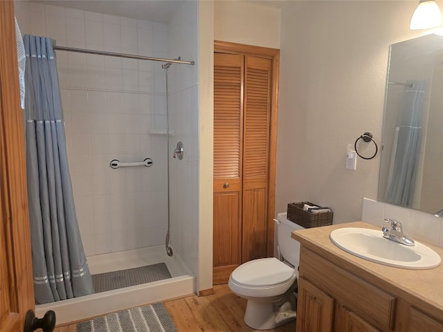 full bath with toilet, wood finished floors, a shower stall, vanity, and a closet