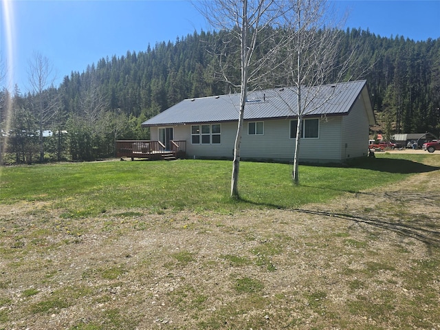 view of property exterior featuring a wooded view, a deck, metal roof, and a yard