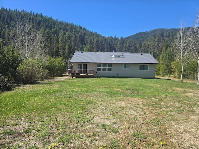 back of property with a wooded view, a deck, a yard, and metal roof
