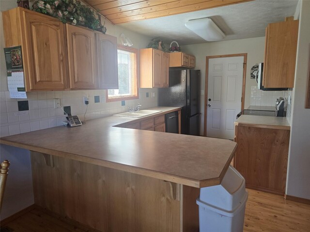 kitchen with tasteful backsplash, a peninsula, light wood-type flooring, black appliances, and a sink