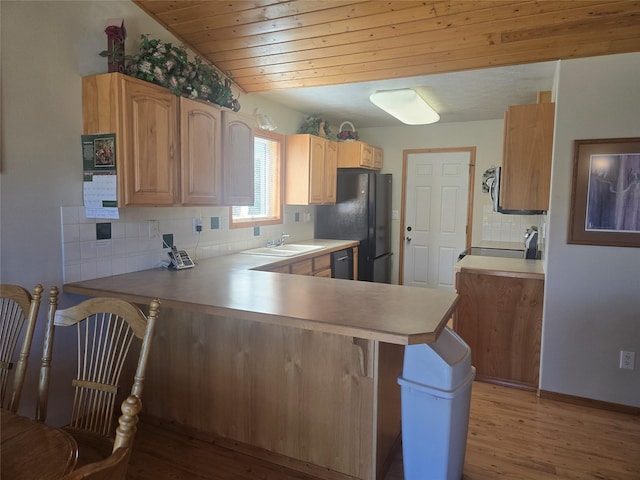kitchen with a peninsula, decorative backsplash, light wood-style floors, black appliances, and a breakfast bar