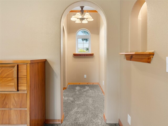 hallway with arched walkways, a chandelier, carpet floors, and baseboards