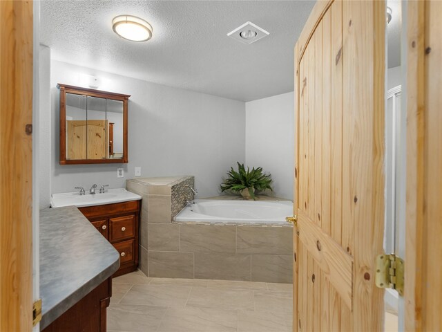 bathroom featuring a garden tub, vanity, and a textured ceiling