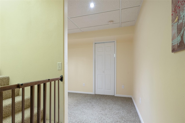 corridor featuring a paneled ceiling, carpet flooring, and baseboards