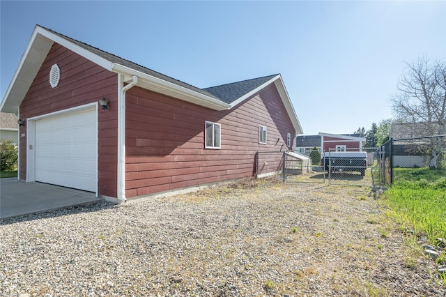 view of side of property featuring fence, concrete driveway, a gate, a garage, and an outbuilding