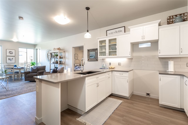 kitchen featuring a sink, a peninsula, glass insert cabinets, white cabinetry, and light wood-type flooring