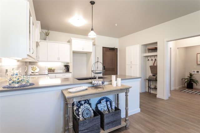 kitchen featuring backsplash, a peninsula, light wood-style flooring, white cabinetry, and a sink