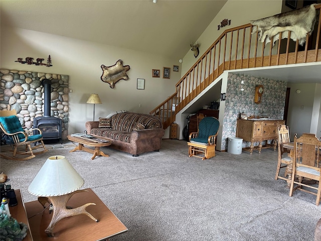 carpeted living room featuring a wood stove, stairway, and high vaulted ceiling