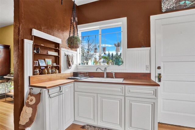 500 34th St NW, Great Falls, MT 59404 - kitchen with a sink, butcher block counters, a wainscoted wall, white cabinets, and wood finished floors