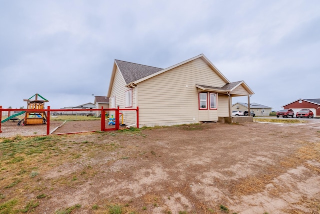 view of side of property with a playground, roof with shingles, and fence