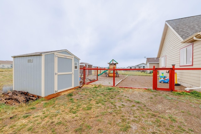 view of yard featuring a storage unit, an outdoor structure, a playground, and fence