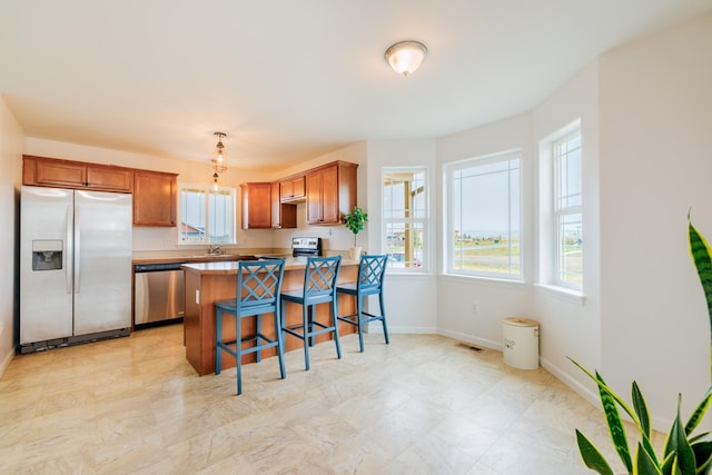 kitchen featuring stainless steel appliances, a peninsula, a breakfast bar, baseboards, and brown cabinets