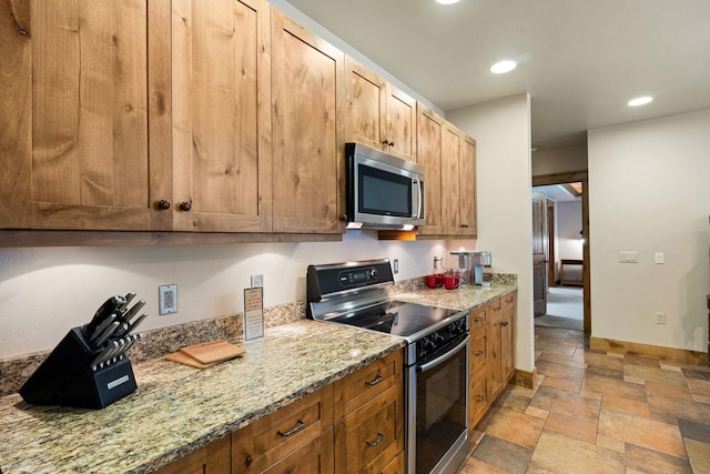 kitchen with appliances with stainless steel finishes, stone tile floors, recessed lighting, light stone countertops, and baseboards