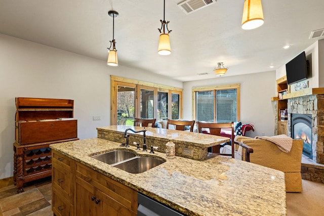 kitchen featuring a sink, decorative light fixtures, light stone countertops, a stone fireplace, and a kitchen island with sink